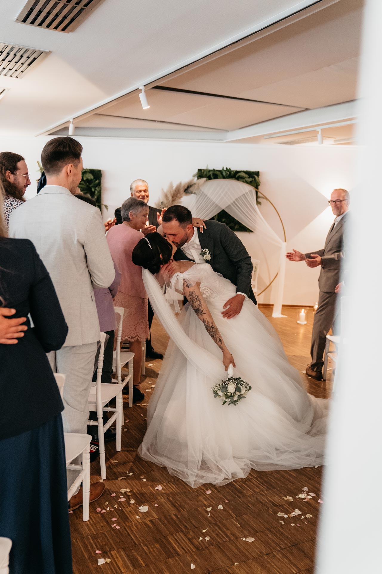 Ein Brautpaar küsst sich bei der Hochzeit, beide lächeln glücklich, in einer weißen Hochzeitsrobe.