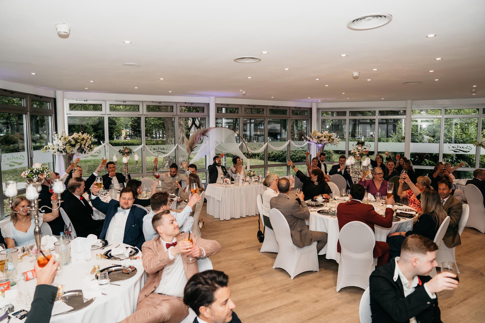 Eine fröhliche Hochzeitsgesellschaft in elegantem Saal, hebt Gläser während eines festlichen Anlasses.