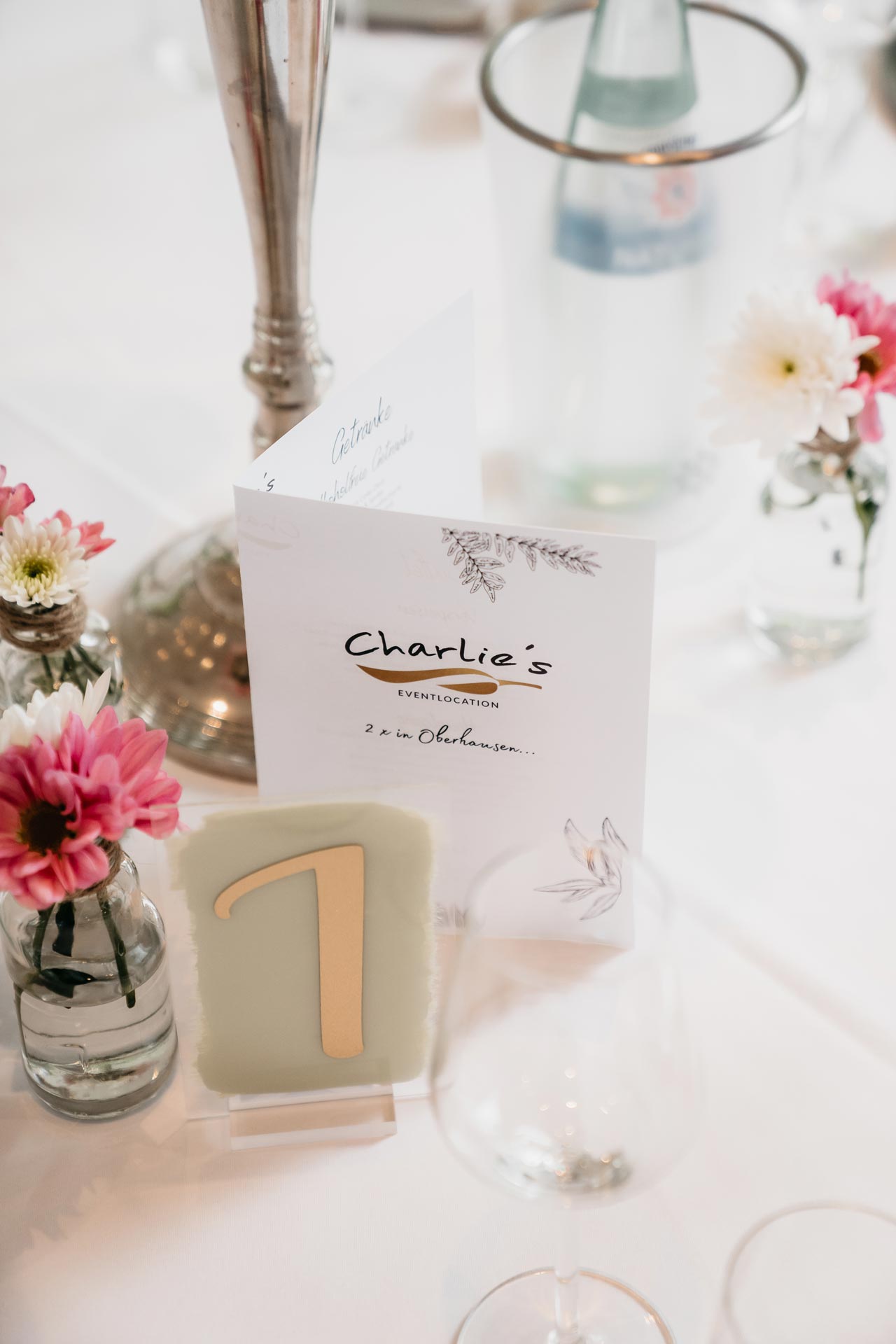 Tischdekoration mit Blumen, Tischkarte "Charlie's" und Tischnummer 1 in elegantem Design.