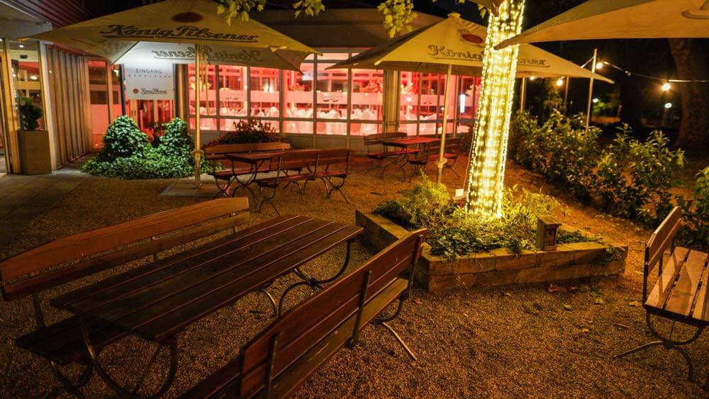 Ein leerer Biergarten bei Nacht mit beleuchtetem Baum und warmem Licht