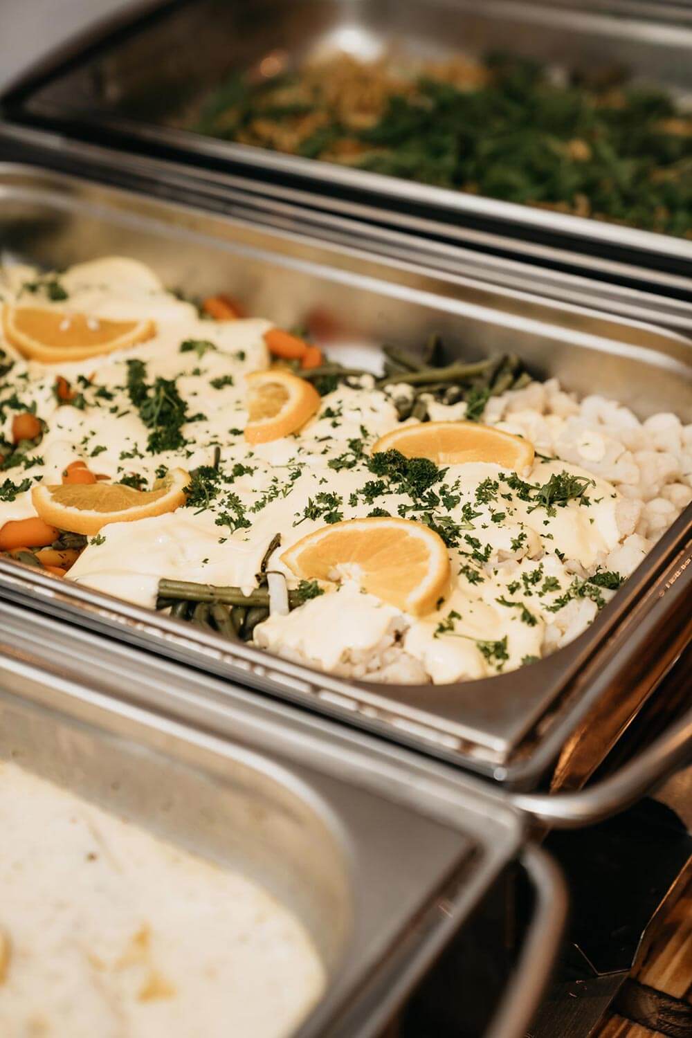 Ein Blech mit Gemüse in heller Sauce garniert mit Orangenscheiben und Kräutern