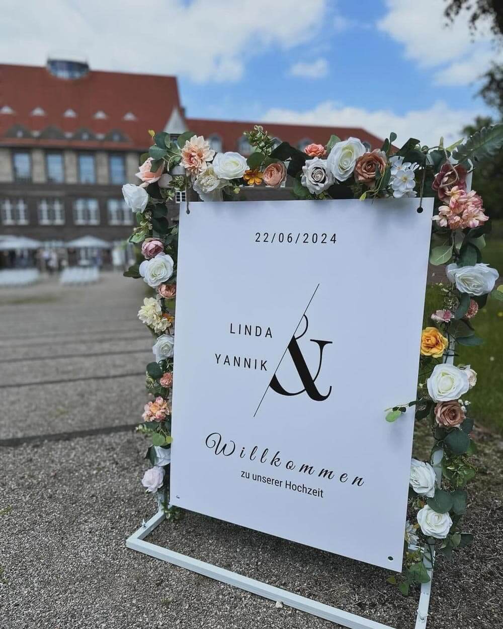 Ein dekoratives Schild mit Blumenrahmen begrüßt Gäste zur Hochzeit von Linda und Yannik