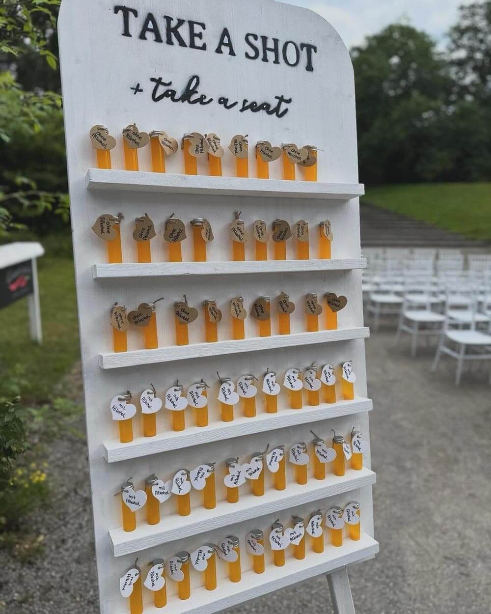Ein weißes Brett mit orangefarbenen Schnapsgläsern und Namensschildern steht im Freien