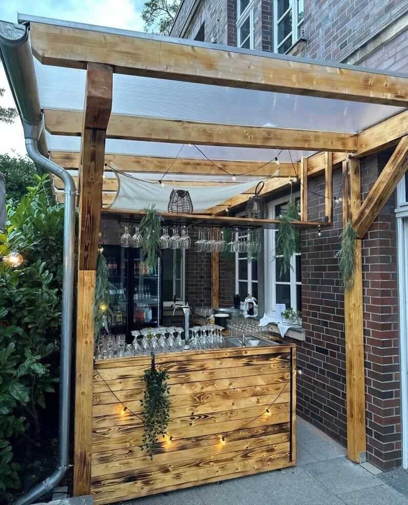 Ein moderner Aussenbereich mit Holzbar und Glasdach, dekoriert mit Gläsern und Lichterkette