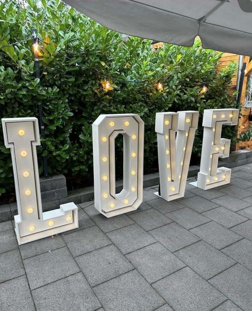 Große weiße Buchstaben mit Lichtern bilden das Wort LOVE auf grauen Fliesen