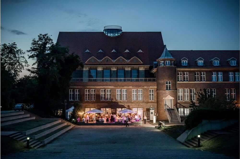Ein rotes Backsteingebäude mit beleuchteten Fenstern und fröhlicher Gesellschaft davor